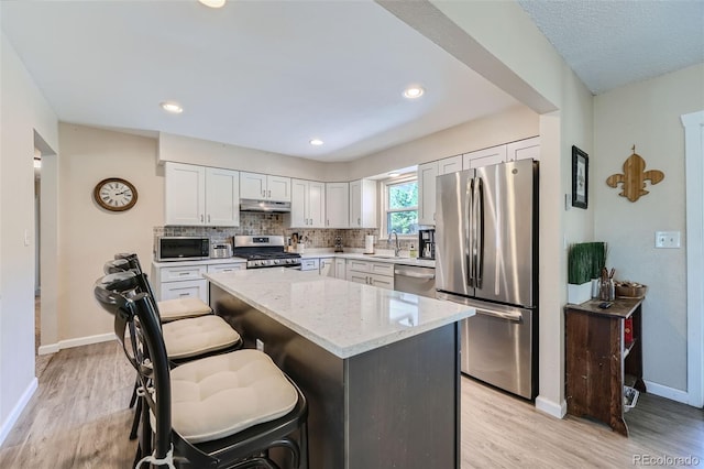 kitchen featuring light wood-type flooring, a breakfast bar area, a kitchen island, appliances with stainless steel finishes, and light stone countertops