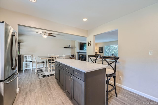 kitchen featuring light stone counters, stainless steel refrigerator, a kitchen island, light wood-type flooring, and ceiling fan