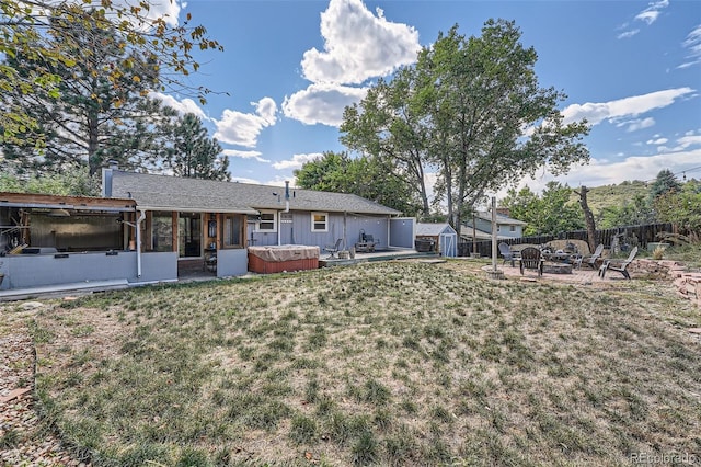 rear view of house featuring a storage unit, an outdoor fire pit, a hot tub, a sunroom, and a yard