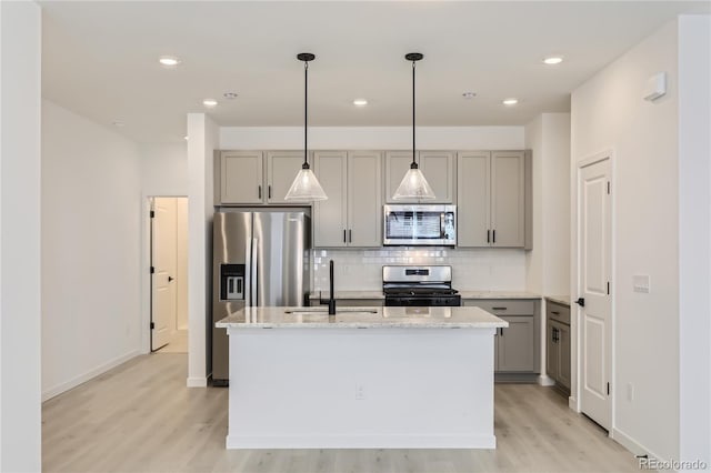 kitchen featuring stainless steel appliances, an island with sink, a sink, and gray cabinetry