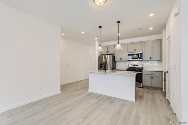 kitchen with decorative light fixtures, appliances with stainless steel finishes, a center island with sink, and gray cabinetry