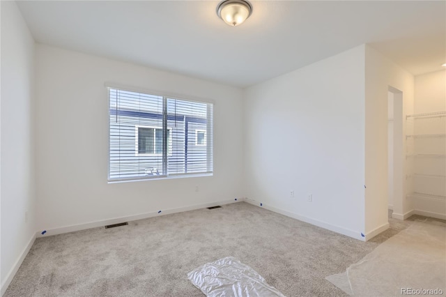 empty room with baseboards, visible vents, and light colored carpet