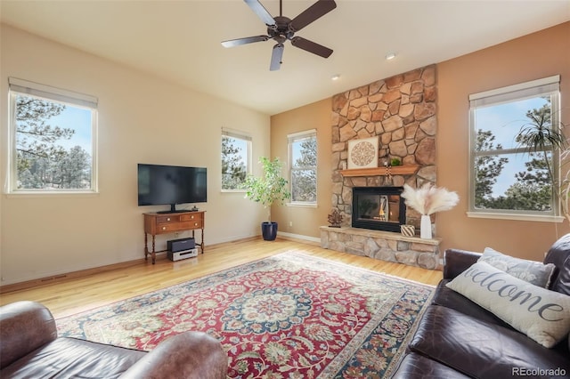 living room with a stone fireplace, wood finished floors, a ceiling fan, and baseboards