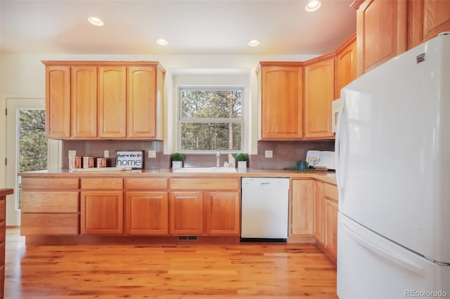 kitchen featuring white appliances, a sink, backsplash, light brown cabinetry, and light wood finished floors