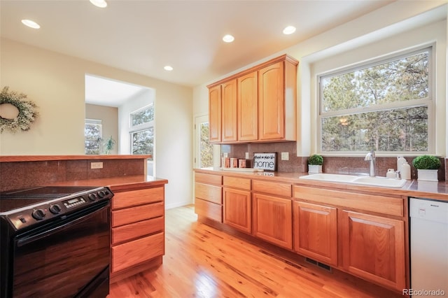 kitchen with black electric range, tasteful backsplash, white dishwasher, a sink, and light wood-type flooring