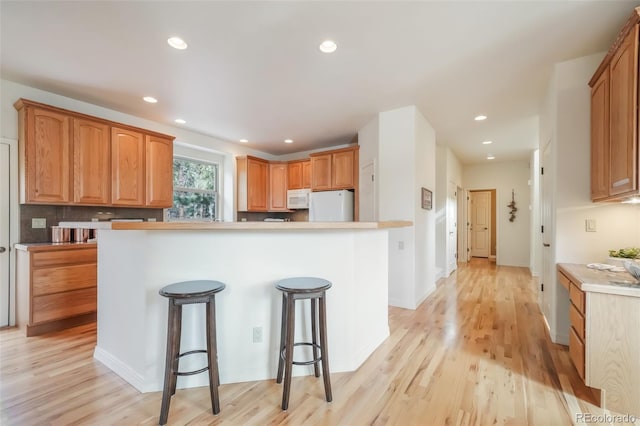 kitchen featuring white appliances, a center island, a breakfast bar, and light wood-style floors