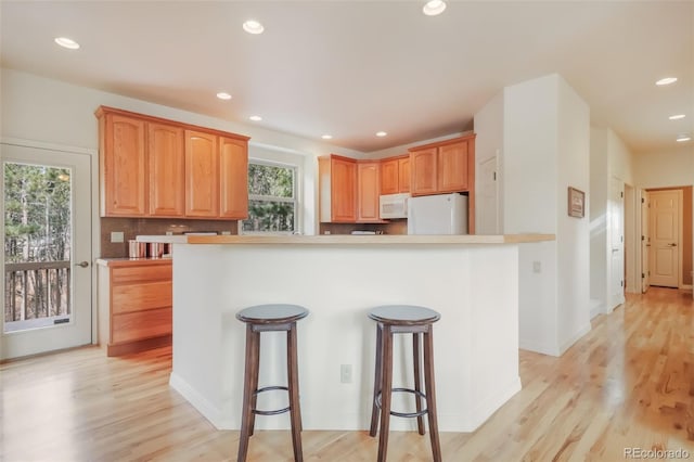 kitchen with white appliances, decorative backsplash, light wood-style floors, a kitchen bar, and recessed lighting