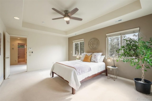 bedroom with light carpet, visible vents, a tray ceiling, and baseboards