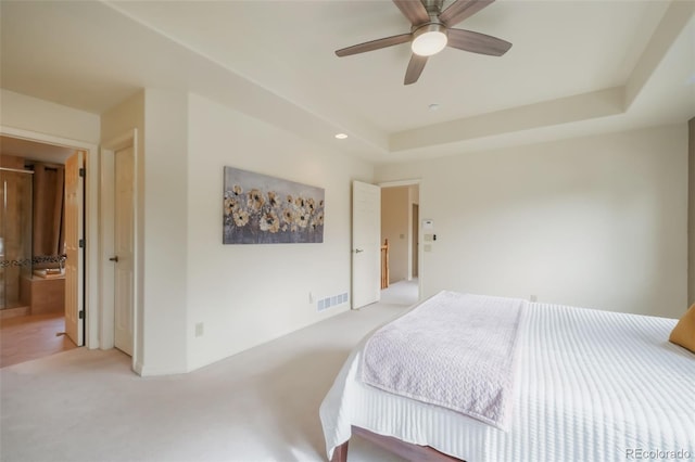 bedroom with ensuite bathroom, light carpet, visible vents, a ceiling fan, and a tray ceiling