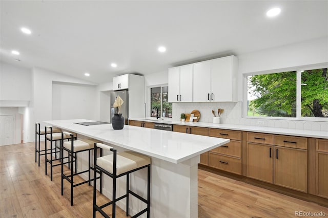 kitchen with stainless steel appliances, decorative backsplash, a sink, light wood-style flooring, and plenty of natural light
