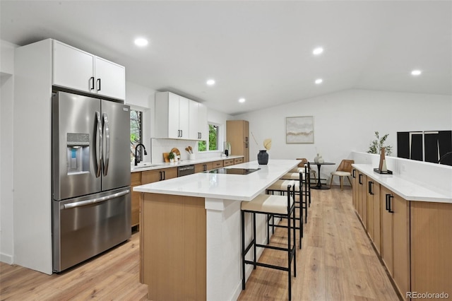 kitchen with stainless steel appliances, a sink, a breakfast bar, a kitchen island, and light wood-style floors