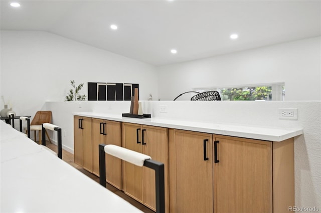 kitchen with recessed lighting, light countertops, lofted ceiling, wood finished floors, and brown cabinetry