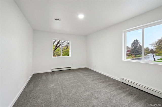 empty room featuring baseboard heating, dark carpet, and baseboards