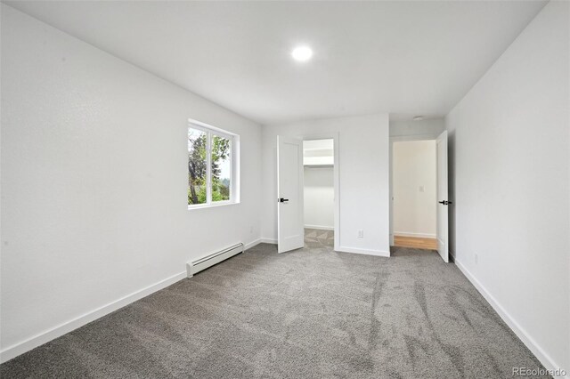 unfurnished bedroom with a baseboard radiator, carpet flooring, baseboards, and a walk in closet