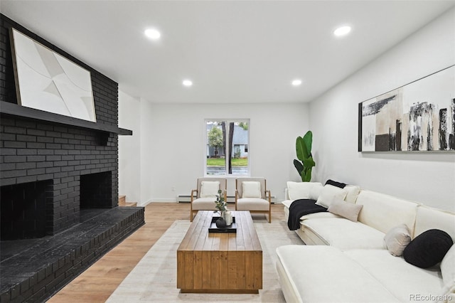 living area with light wood finished floors, baseboard heating, recessed lighting, and a fireplace