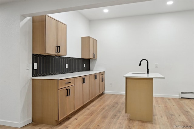 kitchen featuring a sink, backsplash, light wood-style flooring, a center island with sink, and light countertops