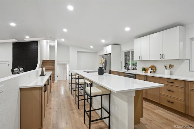 11351 Quivas Way, Denver, CO 80234 - kitchen with appliances with stainless steel finishes, a kitchen bar, backsplash, a large island, and light wood finished floors