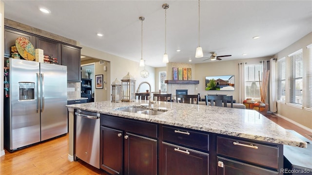 kitchen with decorative light fixtures, appliances with stainless steel finishes, open floor plan, a large fireplace, and a sink