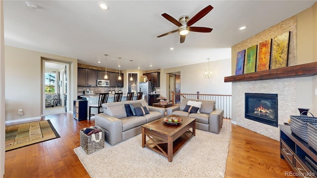 living room featuring ceiling fan with notable chandelier, a glass covered fireplace, light wood-style flooring, and recessed lighting