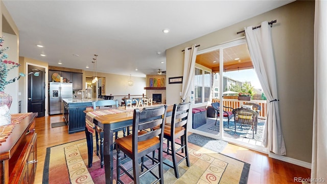 dining room featuring a large fireplace, baseboards, a ceiling fan, light wood-style flooring, and recessed lighting