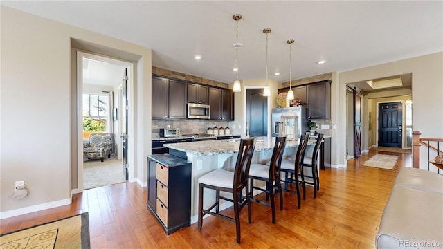 kitchen with a center island, pendant lighting, stainless steel appliances, dark brown cabinetry, and a kitchen breakfast bar