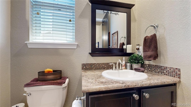 half bathroom with a textured wall, vanity, and toilet