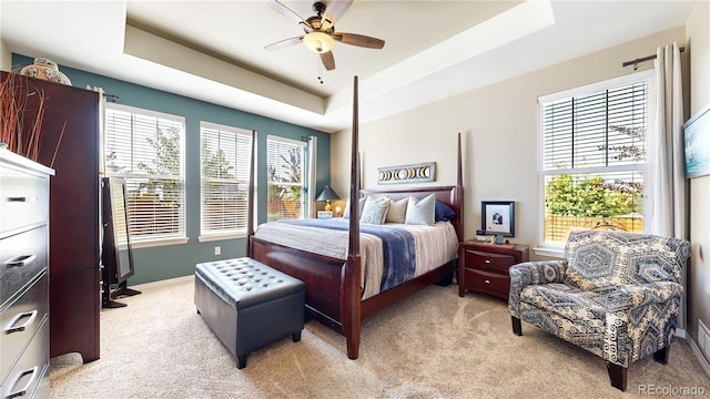 bedroom with a raised ceiling, light carpet, ceiling fan, and baseboards