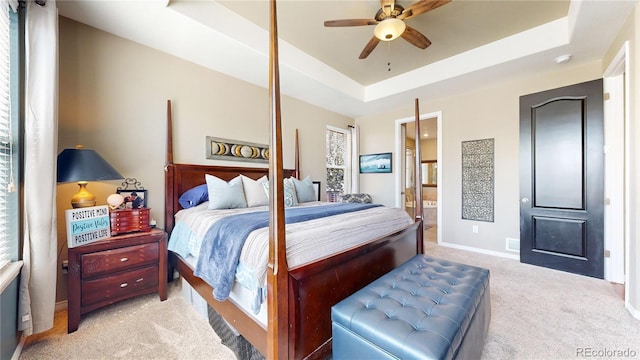 bedroom with ensuite bathroom, light carpet, a ceiling fan, baseboards, and a raised ceiling