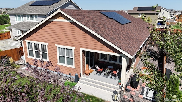 rear view of house with a patio area, fence, solar panels, and roof with shingles