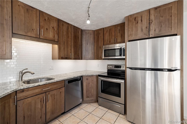 kitchen with light tile patterned flooring, sink, tasteful backsplash, stainless steel appliances, and light stone countertops