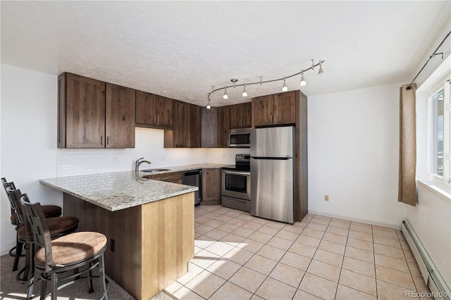 kitchen featuring light tile patterned flooring, tasteful backsplash, a baseboard heating unit, kitchen peninsula, and stainless steel appliances