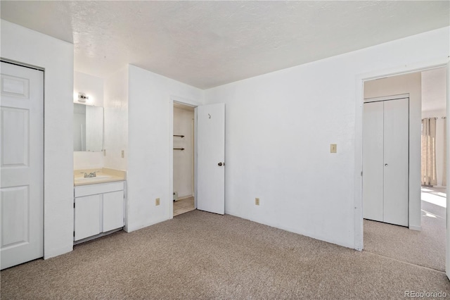 unfurnished bedroom with light colored carpet, connected bathroom, sink, and a textured ceiling