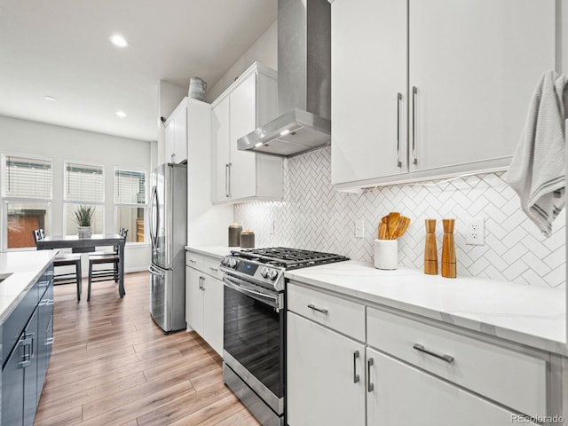 kitchen featuring tasteful backsplash, appliances with stainless steel finishes, wall chimney exhaust hood, white cabinetry, and light wood-style floors