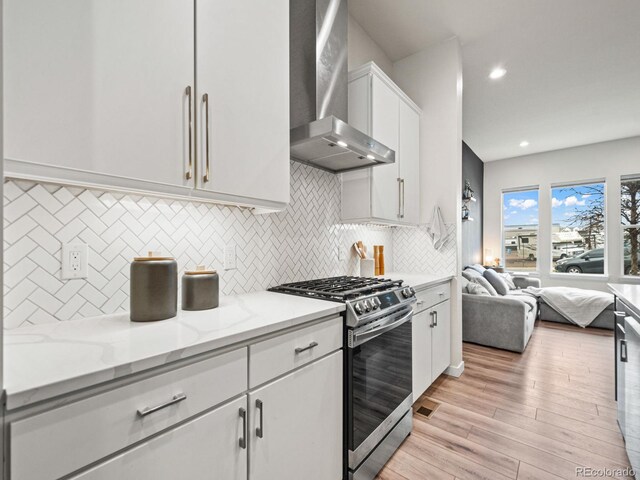 kitchen with stainless steel gas range oven, white cabinetry, open floor plan, wall chimney range hood, and light wood-type flooring