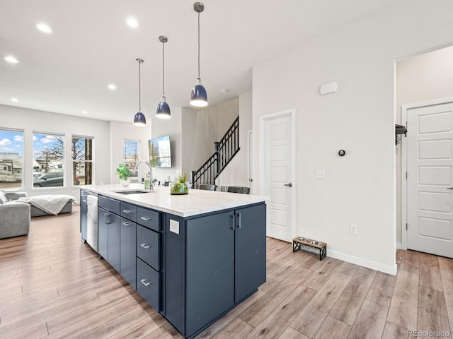 kitchen featuring a sink, an island with sink, light wood finished floors, open floor plan, and stainless steel dishwasher