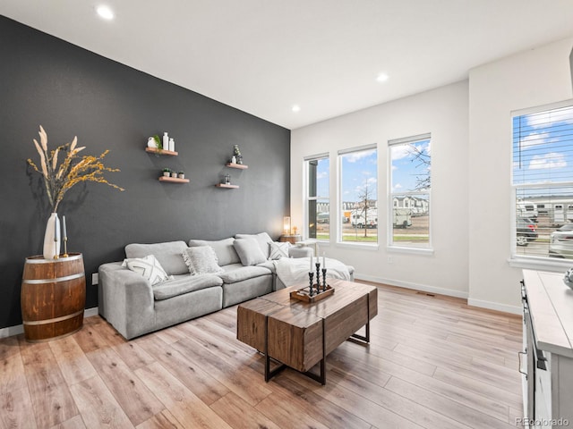 living room featuring light wood-style floors, a healthy amount of sunlight, and an accent wall