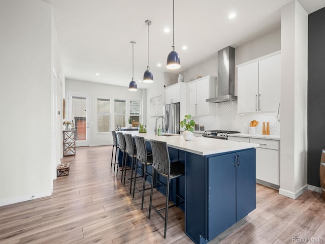 kitchen with wall chimney range hood, light wood-style floors, white cabinets, and decorative backsplash