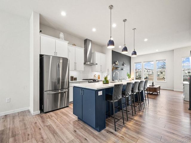 kitchen featuring recessed lighting, a spacious island, wall chimney exhaust hood, light countertops, and appliances with stainless steel finishes