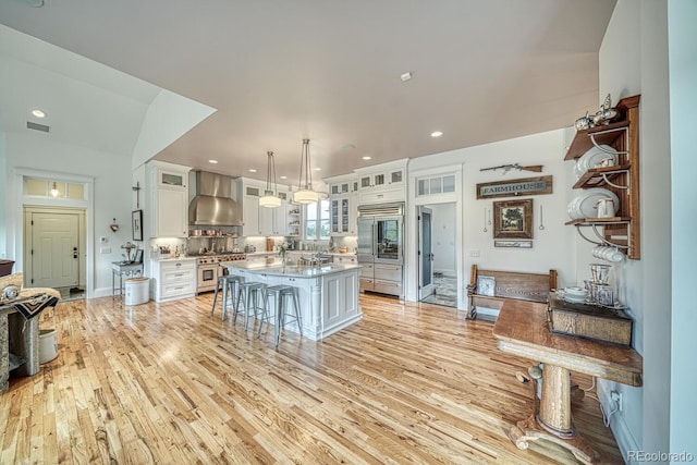 16202 County Road 327, Buena Vista, CO 81211 - kitchen featuring wall chimney range hood, high quality appliances, a kitchen bar, light wood-style flooring, and white cabinetry