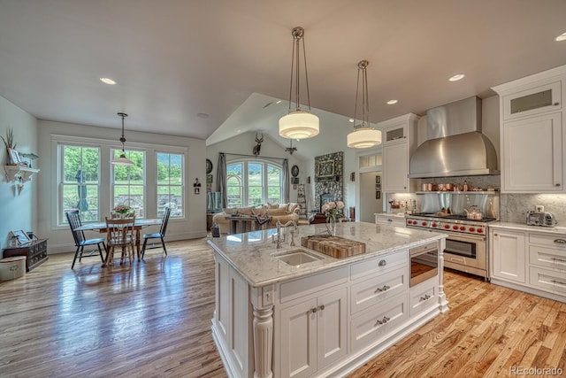 16202 County Road 327, Buena Vista, CO 81211 - kitchen featuring wall chimney range hood, appliances with stainless steel finishes, an island with sink, white cabinetry, and light wood finished floors