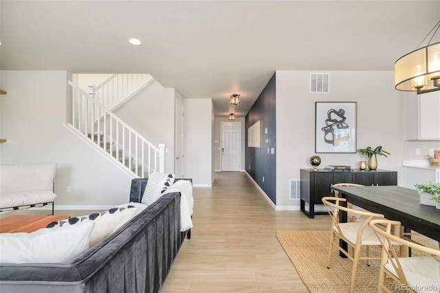 living room featuring light wood-type flooring, stairway, baseboards, and visible vents