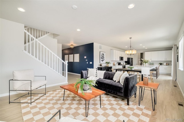 living area featuring a chandelier, light wood finished floors, stairway, and recessed lighting