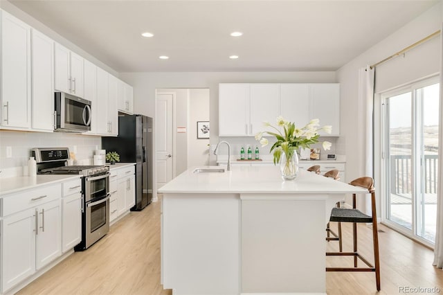 kitchen with light wood finished floors, a kitchen breakfast bar, a kitchen island with sink, stainless steel appliances, and a sink