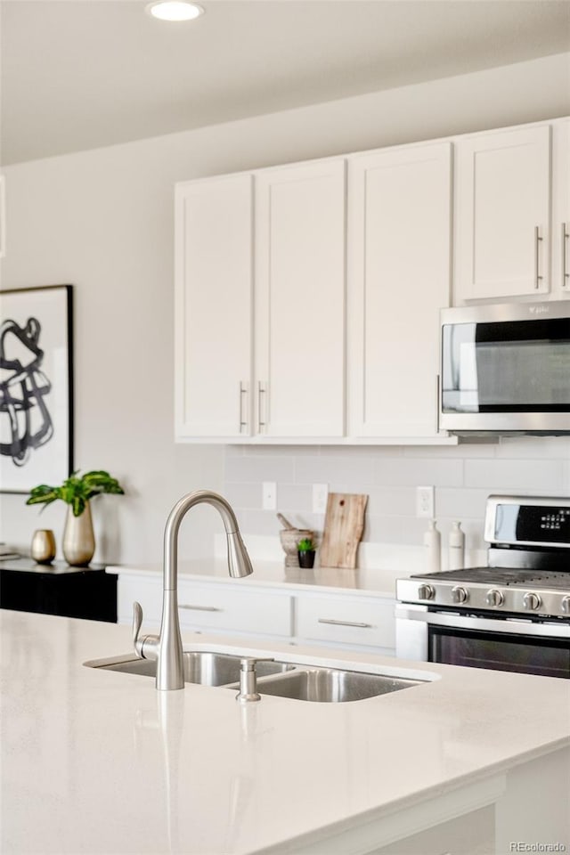 kitchen with tasteful backsplash, appliances with stainless steel finishes, a sink, and white cabinets