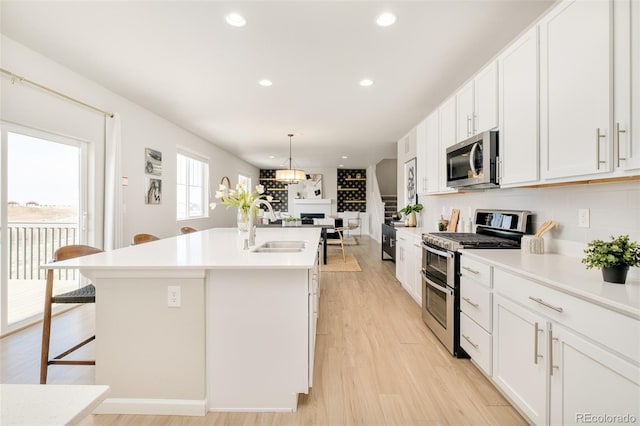 kitchen with a kitchen island with sink, stainless steel appliances, a breakfast bar, a sink, and white cabinets