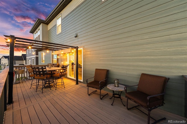 deck at dusk featuring outdoor dining area and a pergola