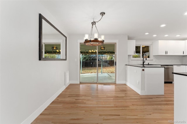 kitchen with pendant lighting, backsplash, white cabinets, light hardwood / wood-style flooring, and a notable chandelier