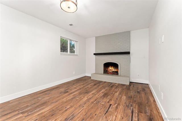 unfurnished living room featuring a brick fireplace and dark wood-type flooring