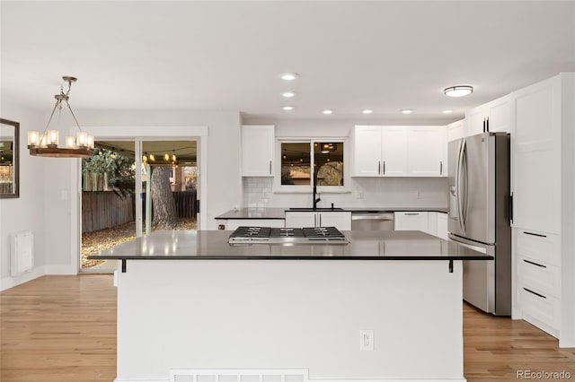 kitchen featuring white cabinets, stainless steel appliances, decorative light fixtures, and a kitchen island