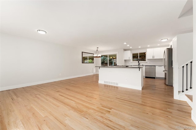 kitchen featuring backsplash, hanging light fixtures, light hardwood / wood-style flooring, appliances with stainless steel finishes, and white cabinetry